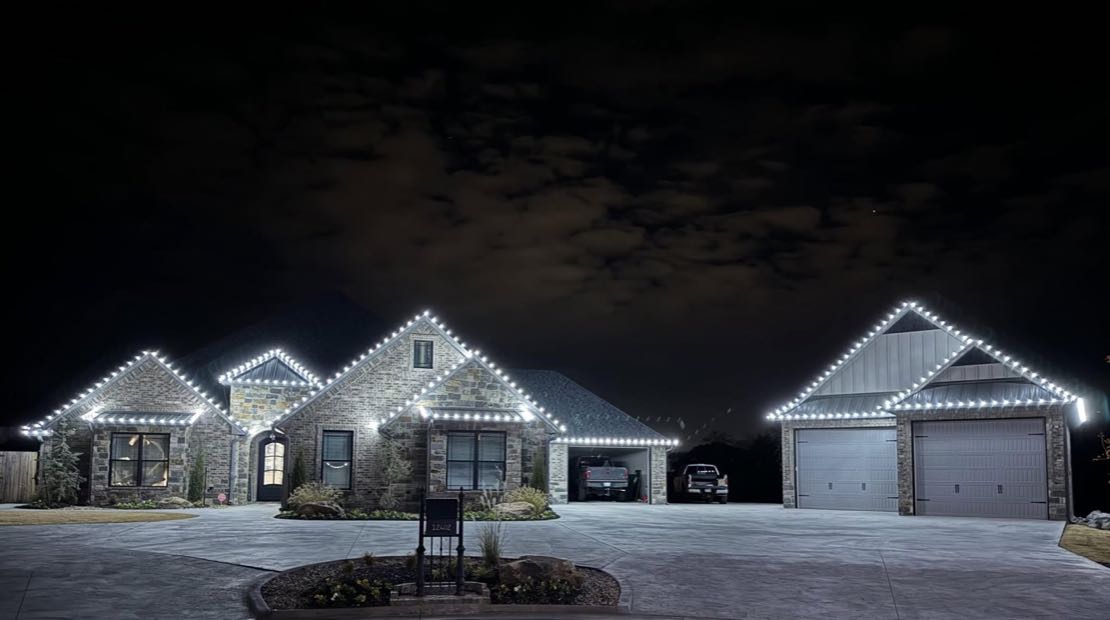 Large stone home with warm white lights outlining every roofline, gable and garage