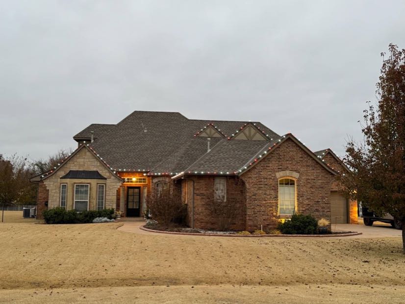 Single-story brick home lit with warm white roofline lights and a glowing entryway