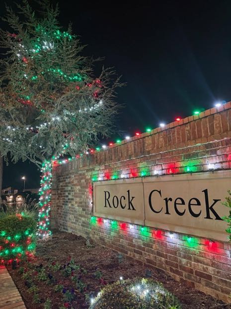 Rock Creek neighborhood entrance sign and evergreen wrapped in red, green and white lights