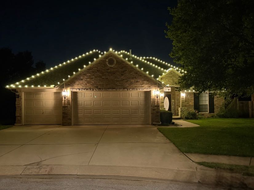 Home with warm white roofline lighting and a lit driveway