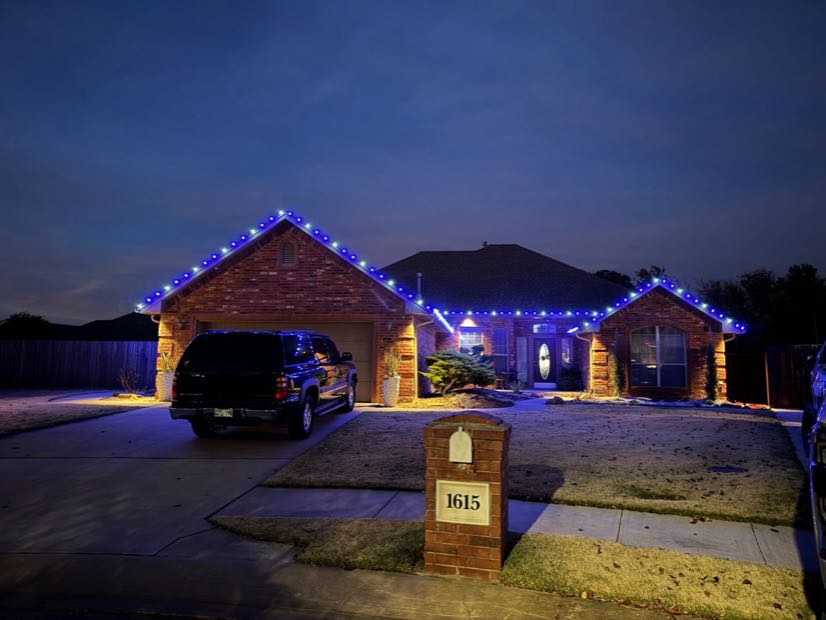Stone home lit with warm white roofline lights at dusk