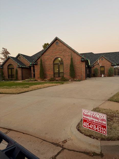 Brick home lit in warm white with a Haubrick yard sign
