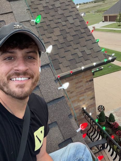 Cameron Haubrick on a roof installing C9 bulbs along the ridge